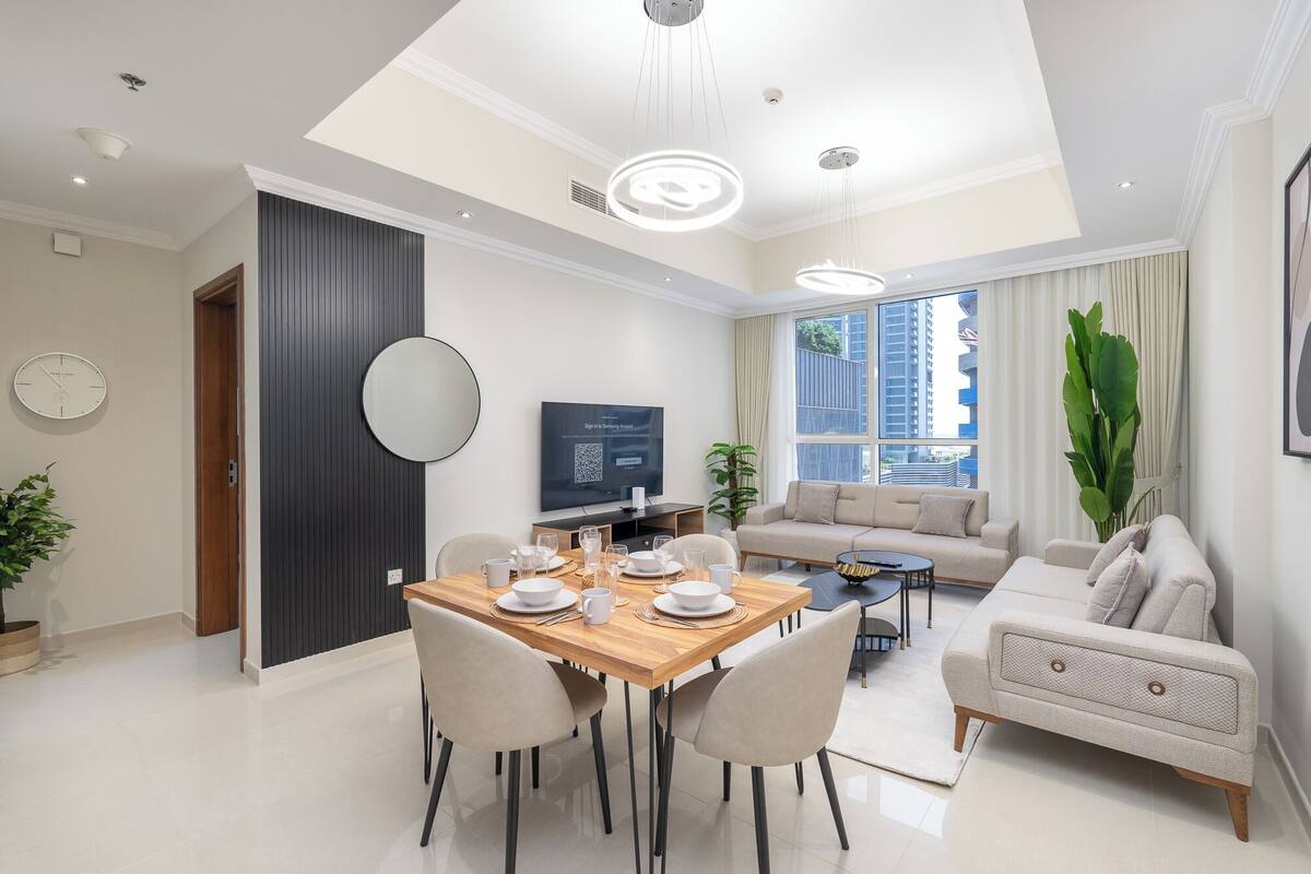 Un salon moderne comprenant un canapé, une table à manger pour quatre personnes, un téléviseur et une grande fenêtre donnant sur des immeubles.