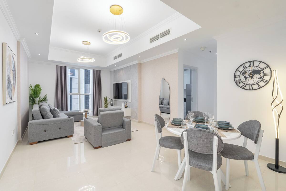 Un salon moderne avec des canapés gris, une table à manger dressée avec des assiettes et des verres, et une grande horloge en forme de carte du monde accrochée au mur.