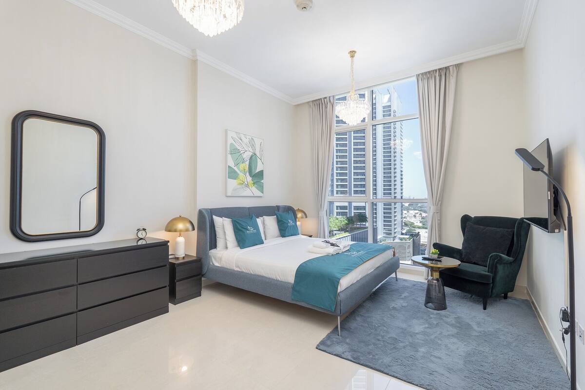 Une chambre à coucher moderne avec un lit, une commode, une chaise et un téléviseur.
