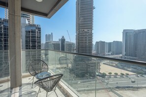 Un balcon doté d’une balustrade en verre, offrant une vue sur un paysage urbain avec de hauts immeubles et des grues de construction.