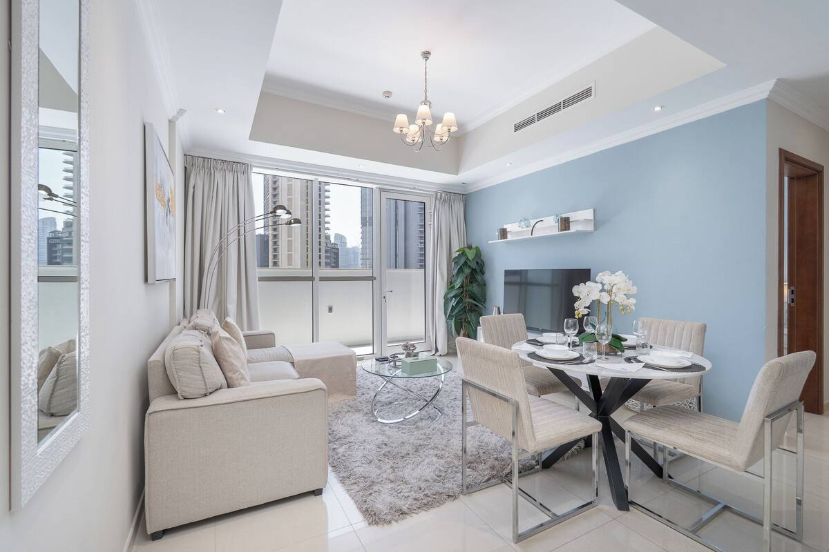 Un salon moderne avec un canapé, une table basse en verre et un coin repas comprenant des chaises et une table dressée pour quatre personnes.