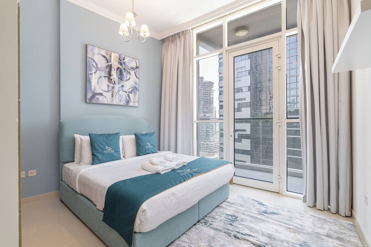 Une chambre moderne avec un grand lit, une vue sur la ville à travers une porte coulissante et un lustre.