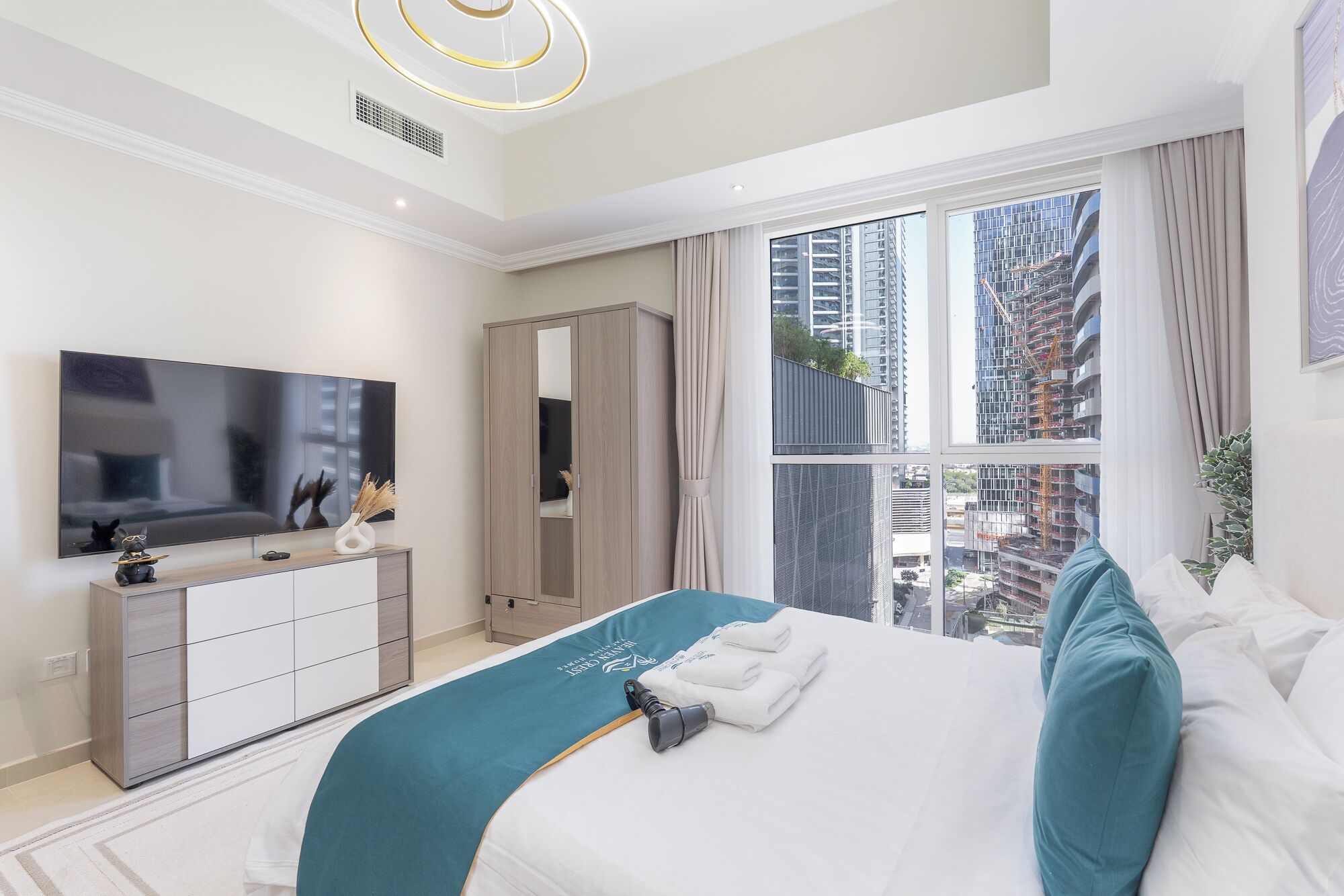 Een moderne hotelkamer met een groot bed, een televisie, een kledingkast en uitzicht op de stad door grote ramen.