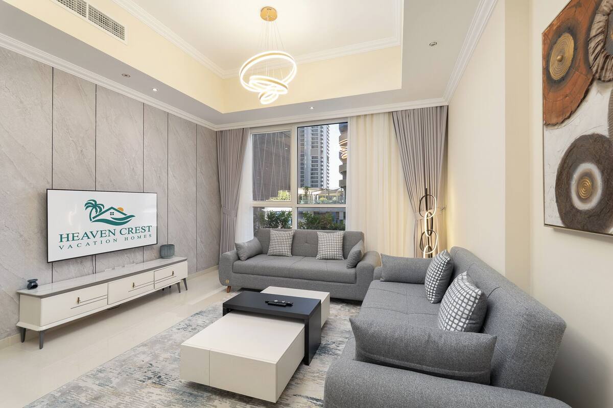 Un salon moderne avec un canapé gris, une table basse blanche et un téléviseur diffusant une publicité pour « Heaven Crest Vacation Homes ».