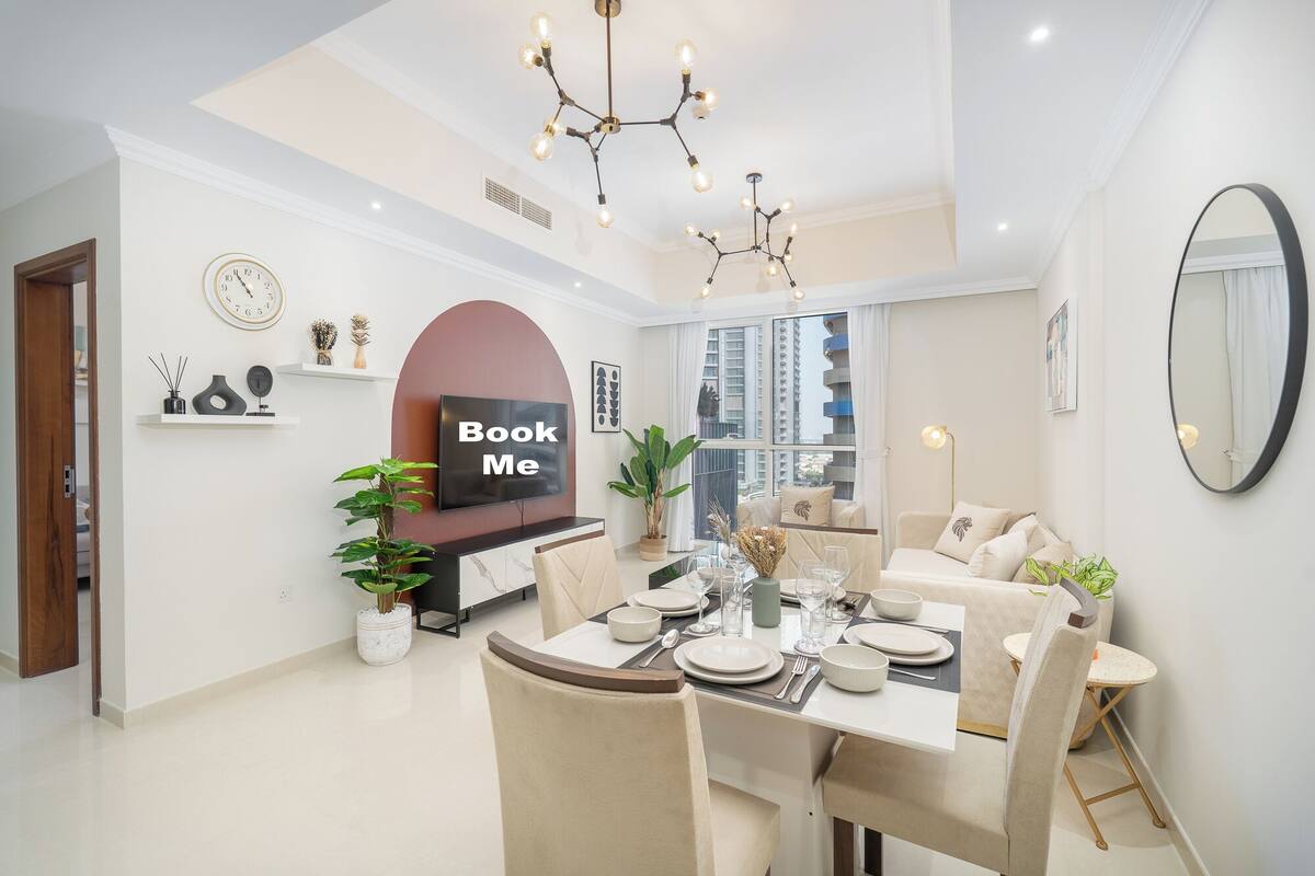 Un espace repas moderne avec une table ronde pour quatre personnes, un grand miroir et un panneau « Réservez-moi » accroché au mur.