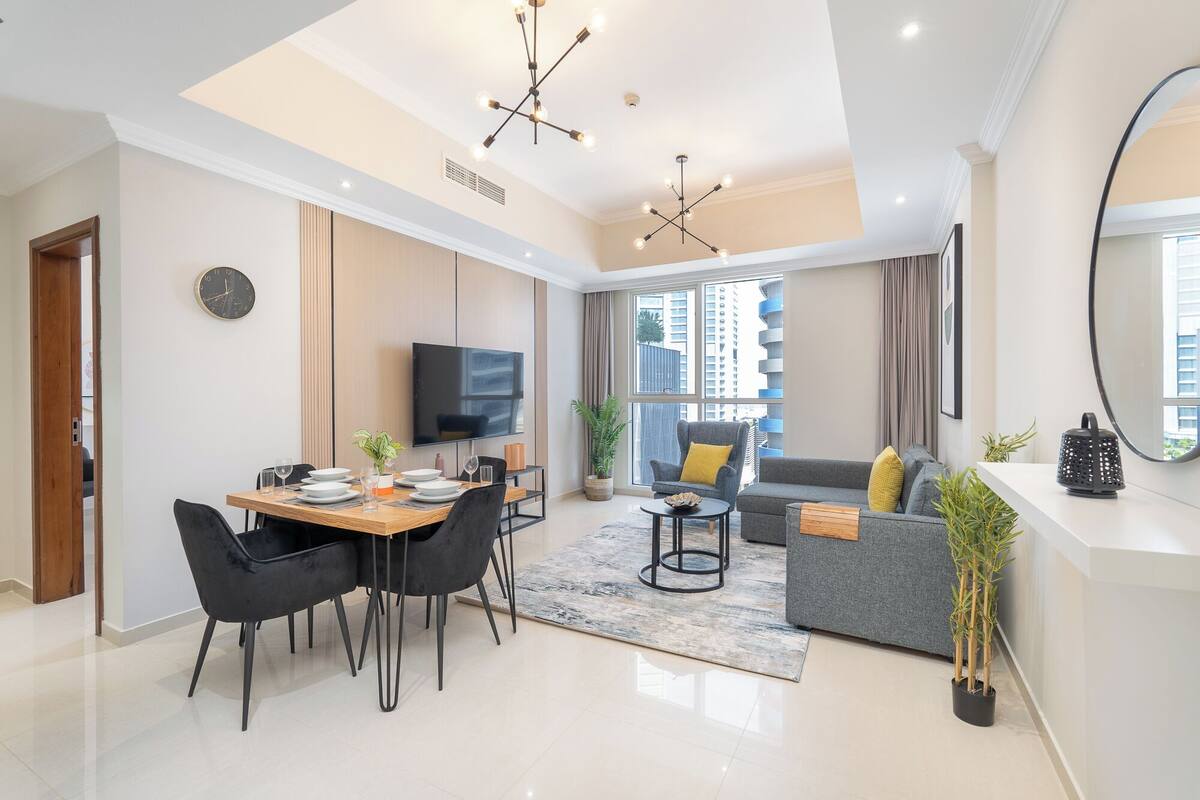 Un salon moderne comprenant un coin repas, un canapé gris et un téléviseur fixé au mur.