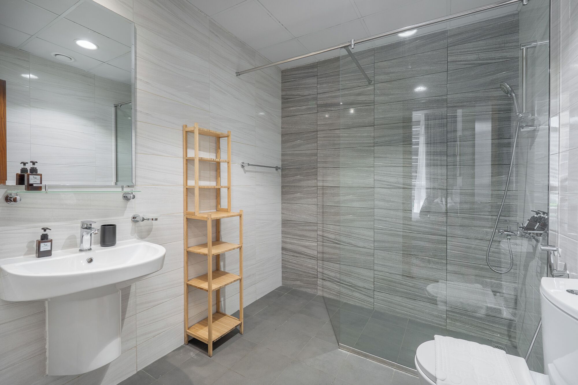 A modern bathroom with a glass shower enclosure, a wooden shelf, and a white sink.