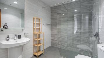A modern bathroom with a glass shower enclosure, a wooden shelf, and a white sink.