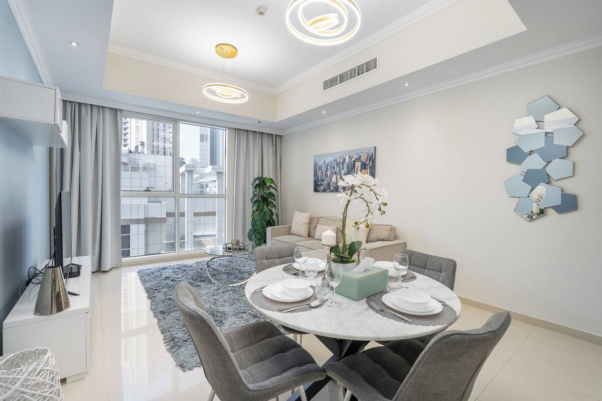 Un espace de repas moderne avec une table ronde pour quatre personnes, un canapé et une vue sur la ville à travers de grandes fenêtres.
