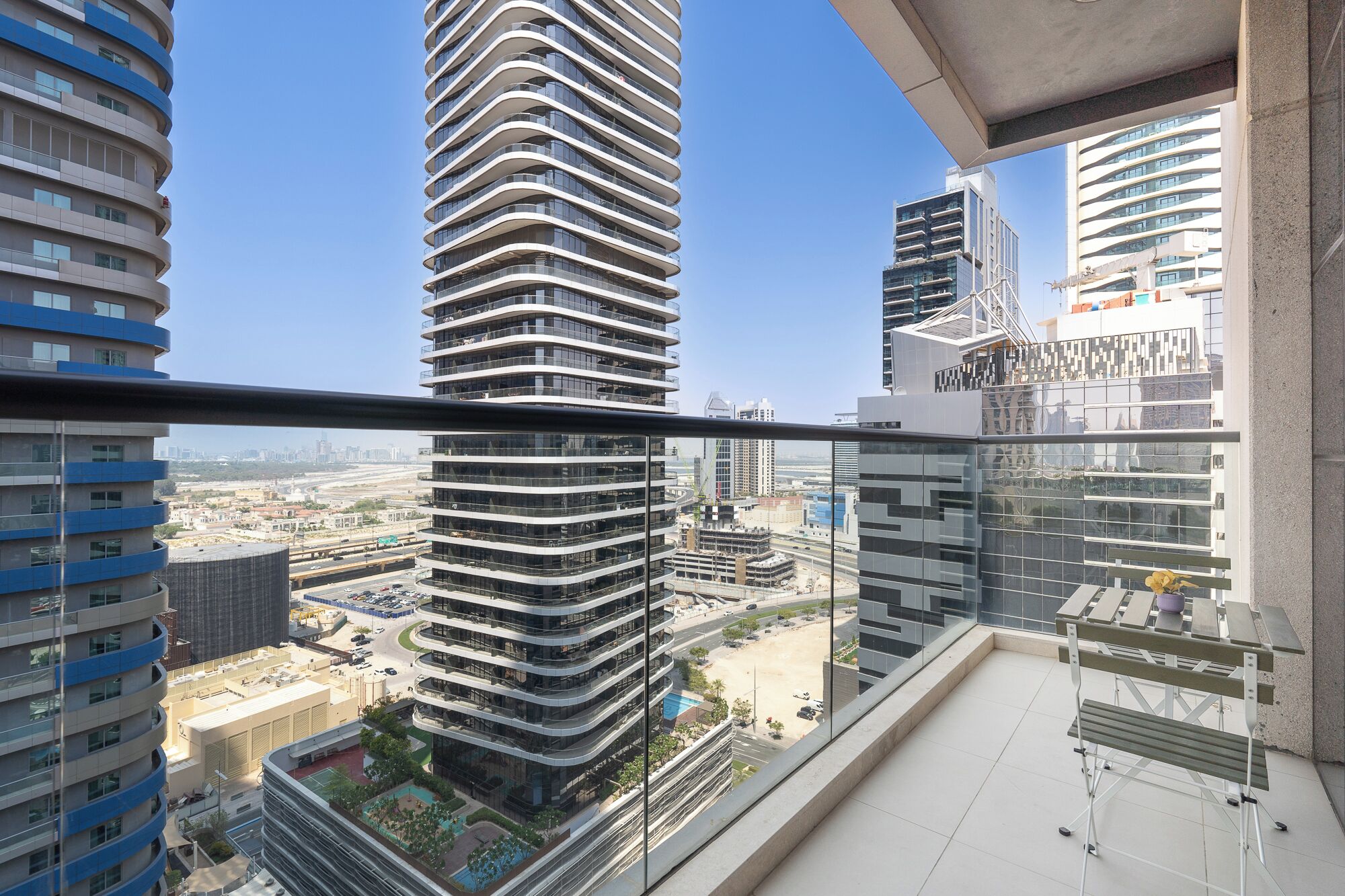 A high-rise building with a curved facade, multiple balconies, and a view of a cityscape with other tall buildings and a road.