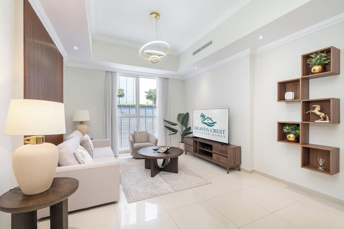 Un salon moderne avec un canapé, une table basse et un téléviseur. Il y a une grande fenêtre avec des rideaux, une plante et une enseigne indiquant « Heaven Crest Vacation Homes ».
