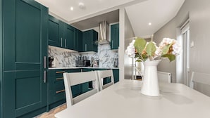A modern kitchen with teal cabinets, a marble backsplash, and a white dining table with chairs.