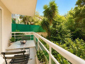 Un balcon avec une table et des chaises, entouré de verdure et d’une clôture verte.