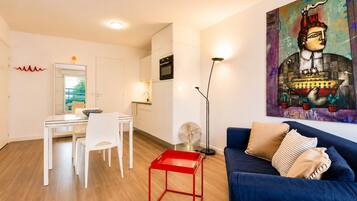 A modern living room with a blue sofa, a red side table, and a dining area with a white table and chairs.