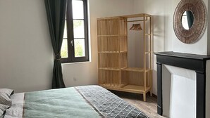 Ein Schlafzimmer mit einem Bett, einem Kleiderschrank, einem Spiegel und einem Fenster mit Vorhängen.