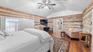 A bedroom with a large bed, a ceiling fan, a TV, and a cozy seating area with a sofa and chairs. - Historic Augusta Cabin | Wine Country & Fire Pit (Augusta)