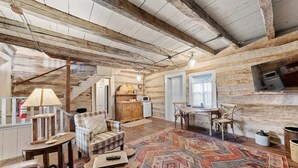 A rustic interior with exposed wooden beams, a checkered sofa, a patterned rug, and a dining area with a table and chairs. - Historic Augusta Cabin | Wine Country & Fire Pit (Augusta)