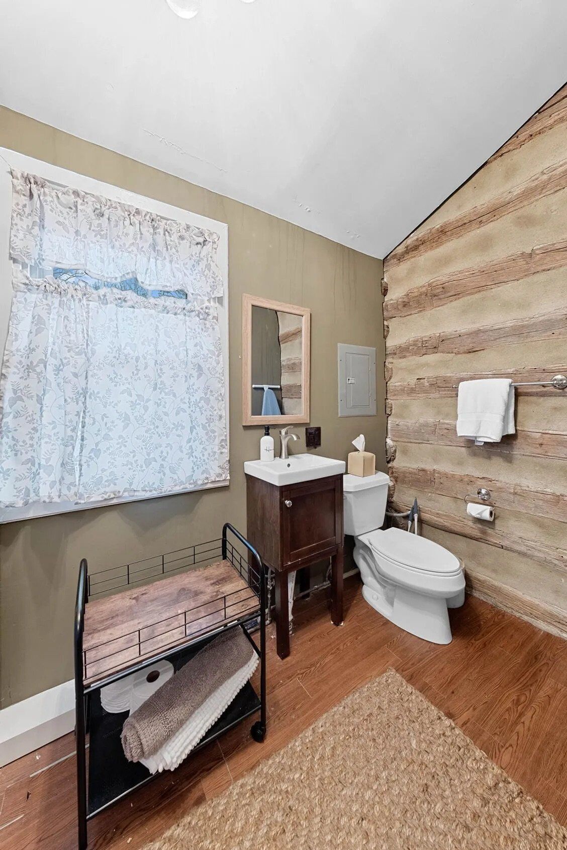 Un baño con piso de madera, un lavamanos, un inodoro, un espejo y un perchero para toallas.