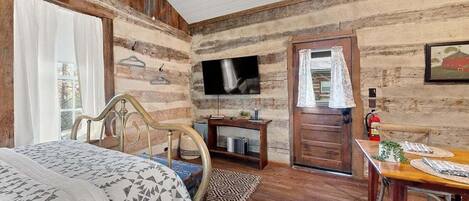 A rustic room with a wooden bed, a television, a wooden dining table, and a small side table.