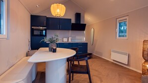 A modern kitchen with dark blue cabinets, a white countertop, and a central island. There is a built-in oven and microwave, a hanging light fixture, and a window with a view of trees. - Luxury Wellness Lodge Hottub Sallandse Heuvelrug Hellendoorn - Trix (Haarle)