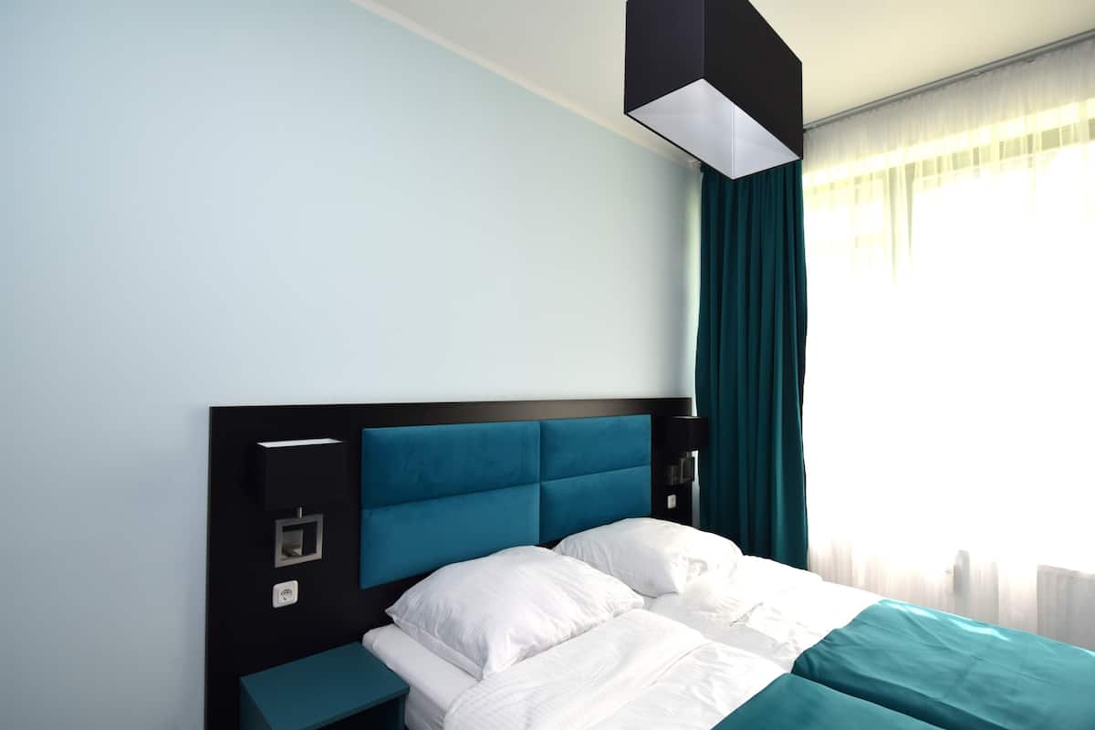 A modern hotel room with a large bed, a nightstand, and a window with curtains.