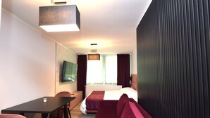 A modern hotel room with a bed, a sofa, a desk, and a TV. - stay with legends (Hamburg)