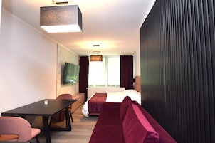 Una habitación de hotel moderna con cama, sofá, escritorio y televisión.