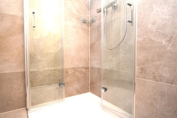 A glass-enclosed shower with a handheld showerhead and a wall-mounted faucet. - stay with legends (Hamburg)