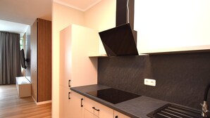 A modern kitchen with a black induction cooktop, a built-in oven, and a stainless steel sink. There is a wooden panel divider and a bench in the adjacent room. - stay with legends (Hamburg)