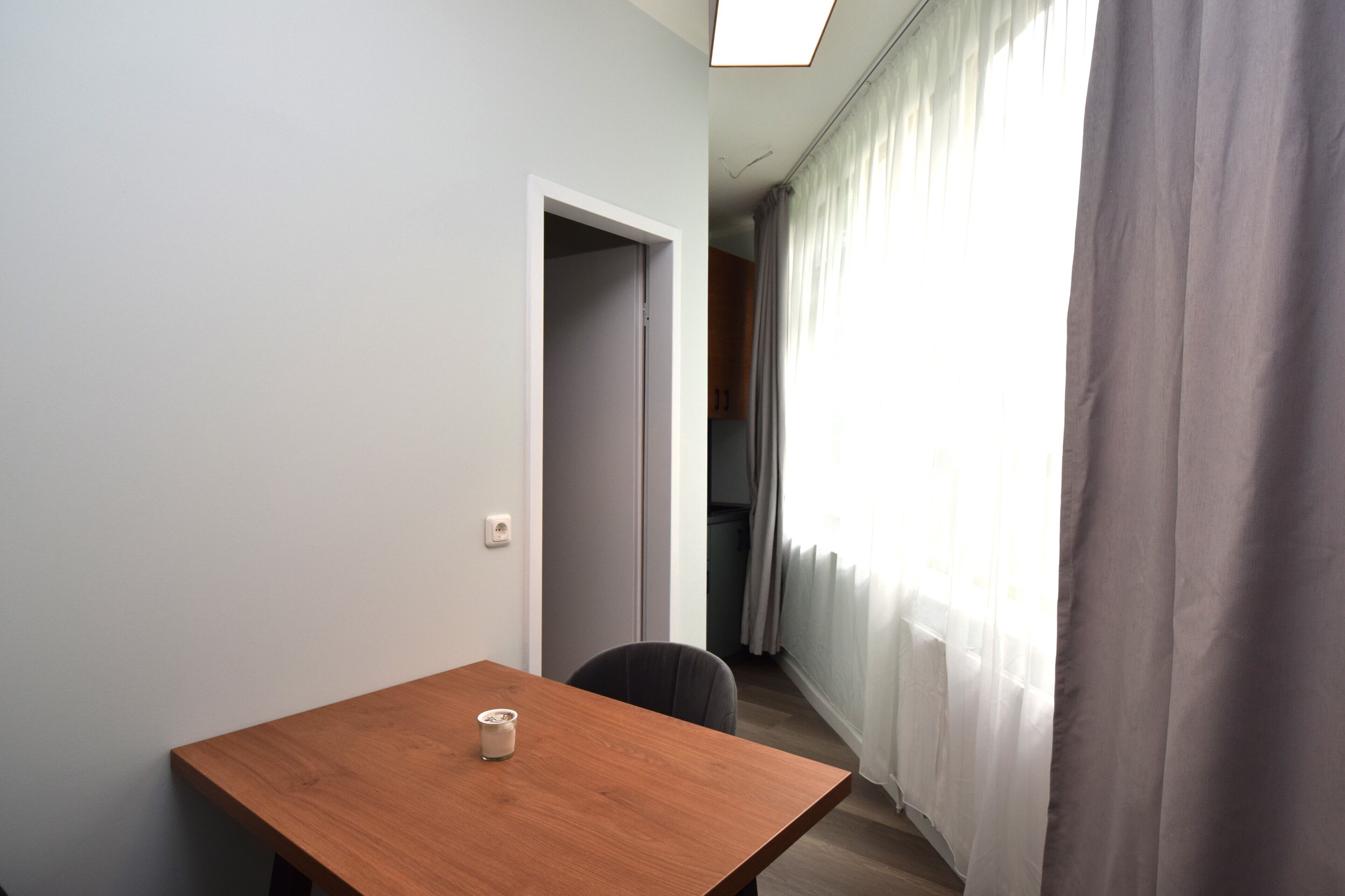 Ein schlichter Raum mit Holztisch, Stuhl und einer Tür zu einem anderen Zimmer.