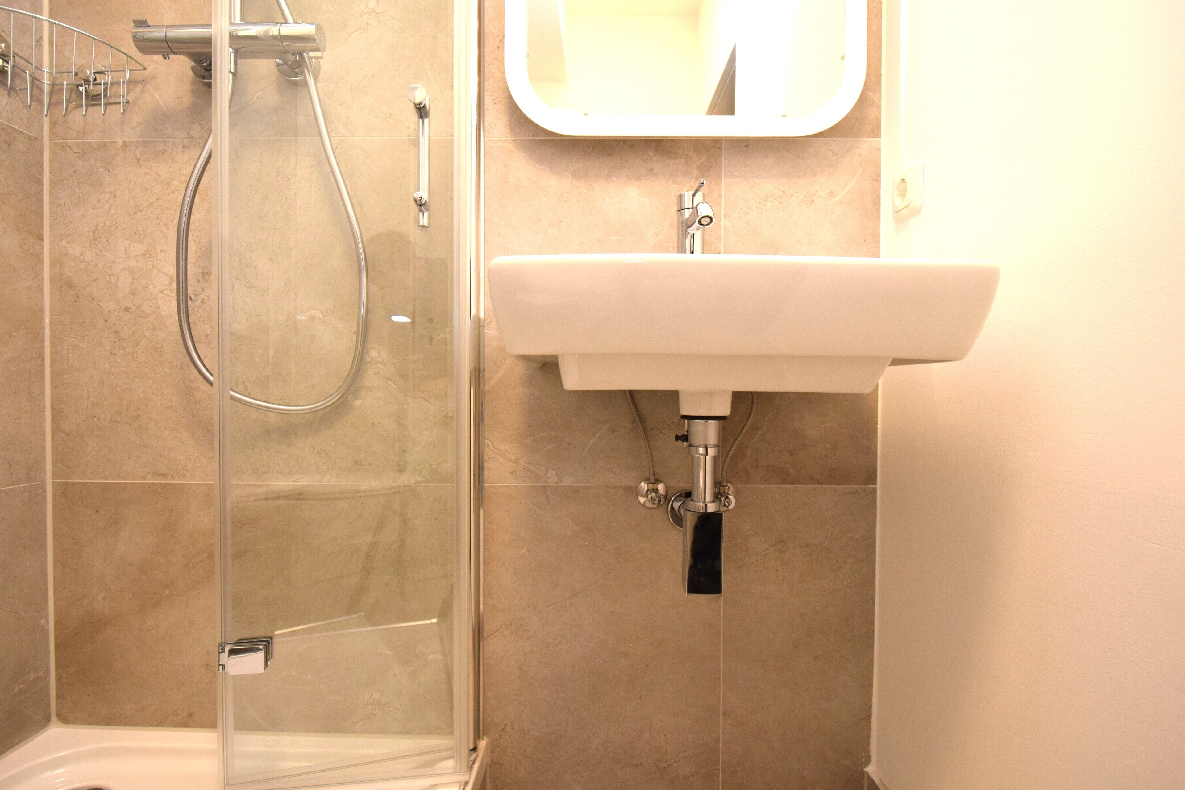 Un baño con ducha de vidrio, un lavamanos blanco y un espejo sobre el lavamanos.
