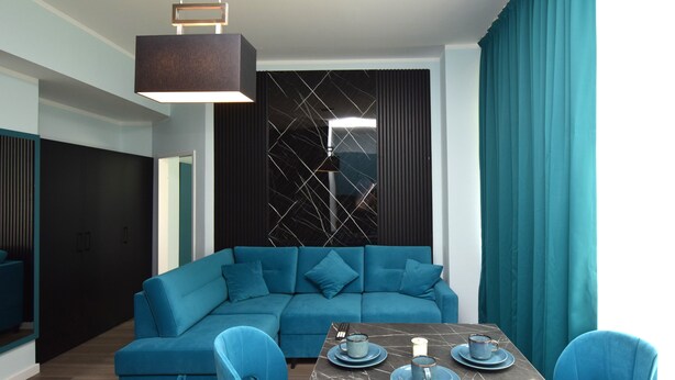 A modern living room with a sectional sofa, a dining table with blue plates and cups, and teal curtains. - stay with legends (Hamburg)