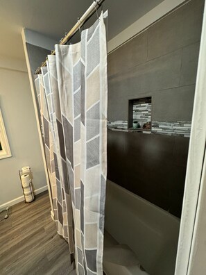 A bathroom with a shower curtain, a towel rack, and a wall-mounted shelf with toiletries. - Cozy 3-bedroom house in fabulous Decatur , AC, WiFi (Decatur)