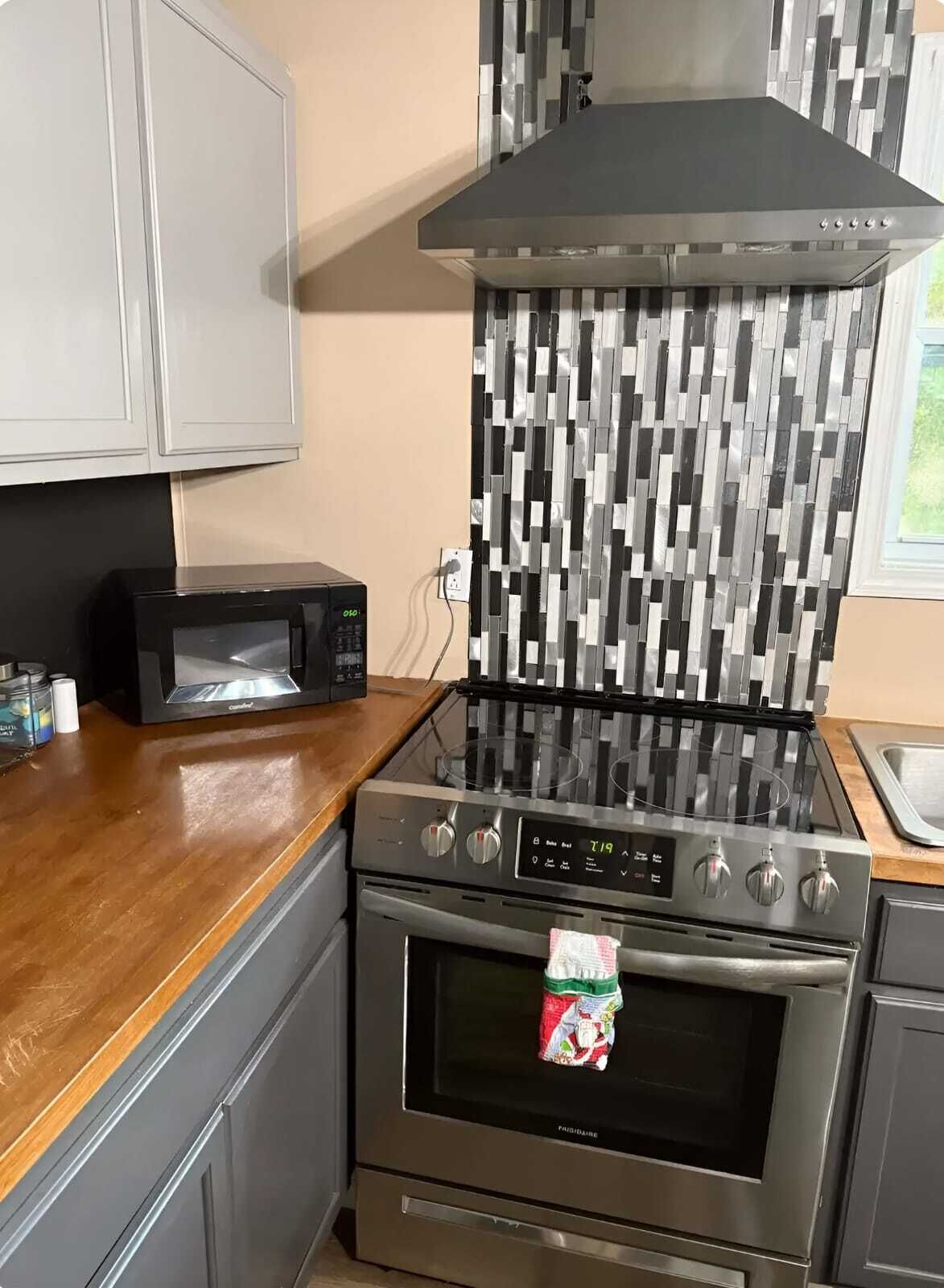 Une cuisine équipée d’un four à micro-ondes, d’une cuisinière et d’un plan de travail recouvert de carreaux.