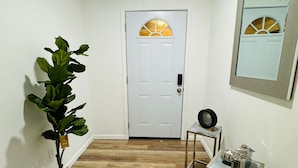 A hallway with a white door, a potted plant, a small table with a vintage radio, and a mirror on the wall. - Cozy 3-bedroom house in fabulous Decatur , AC, WiFi (Decatur)