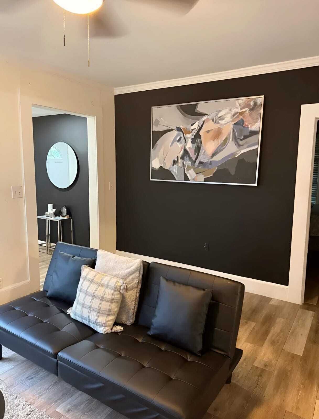Een moderne woonkamer met een leren zwarte bank, een ronde spiegel en een groot abstract schilderij aan de muur.