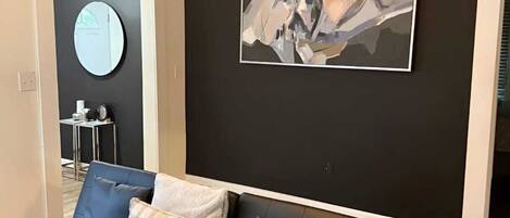 Een moderne woonkamer met een leren zwarte bank, een ronde spiegel en een groot abstract schilderij aan de muur.