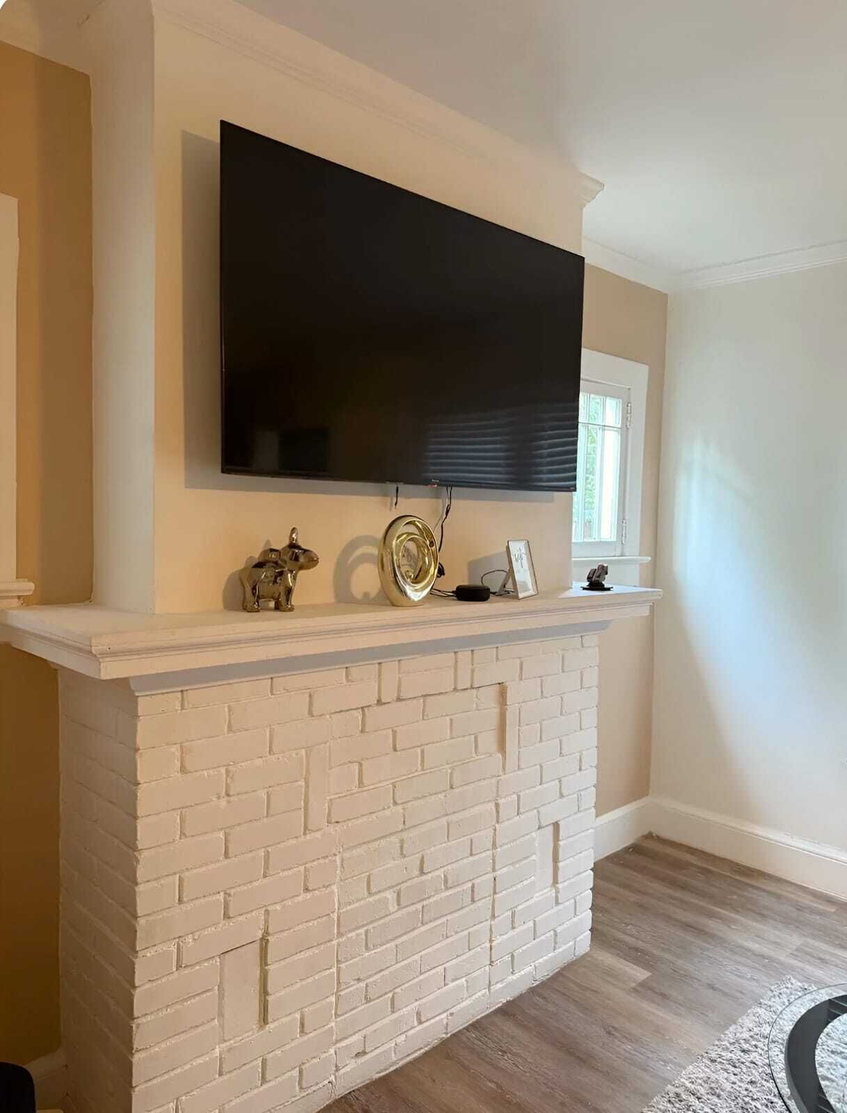 A living room with a white brick fireplace, a mounted flat-screen TV, and a small decorative item on the mantel.