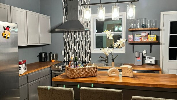 A modern kitchen with a central island, bar stools, and a coffee station.