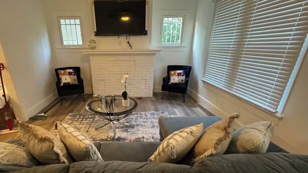 A living room with a gray sofa, a coffee table, two black chairs, a fireplace, and a TV mounted on the wall. - Cozy 3-bedroom house in fabulous Decatur , AC, WiFi (Decatur)