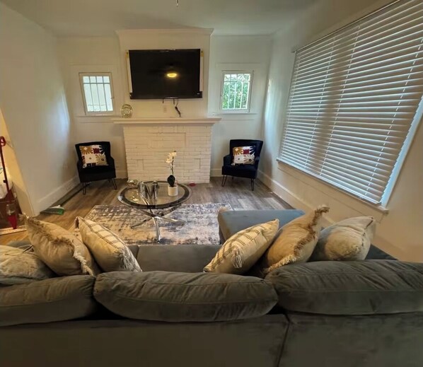 A living room with a gray sofa, a coffee table, two black chairs, a fireplace, and a TV mounted on the wall. - Cozy 3-bedroom house in fabulous Decatur , AC, WiFi (Decatur)