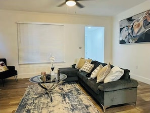 A living room with a dark grey sectional sofa, a glass coffee table, a patterned rug, and a ceiling fan. - Cozy 3-bedroom house in fabulous Decatur , AC, WiFi (Decatur)