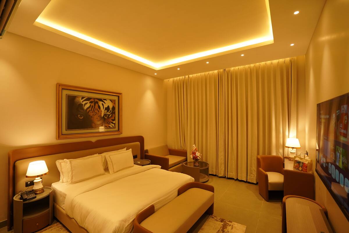 A hotel room with a bed, bedside tables, a sofa, a TV, and a large window with curtains.