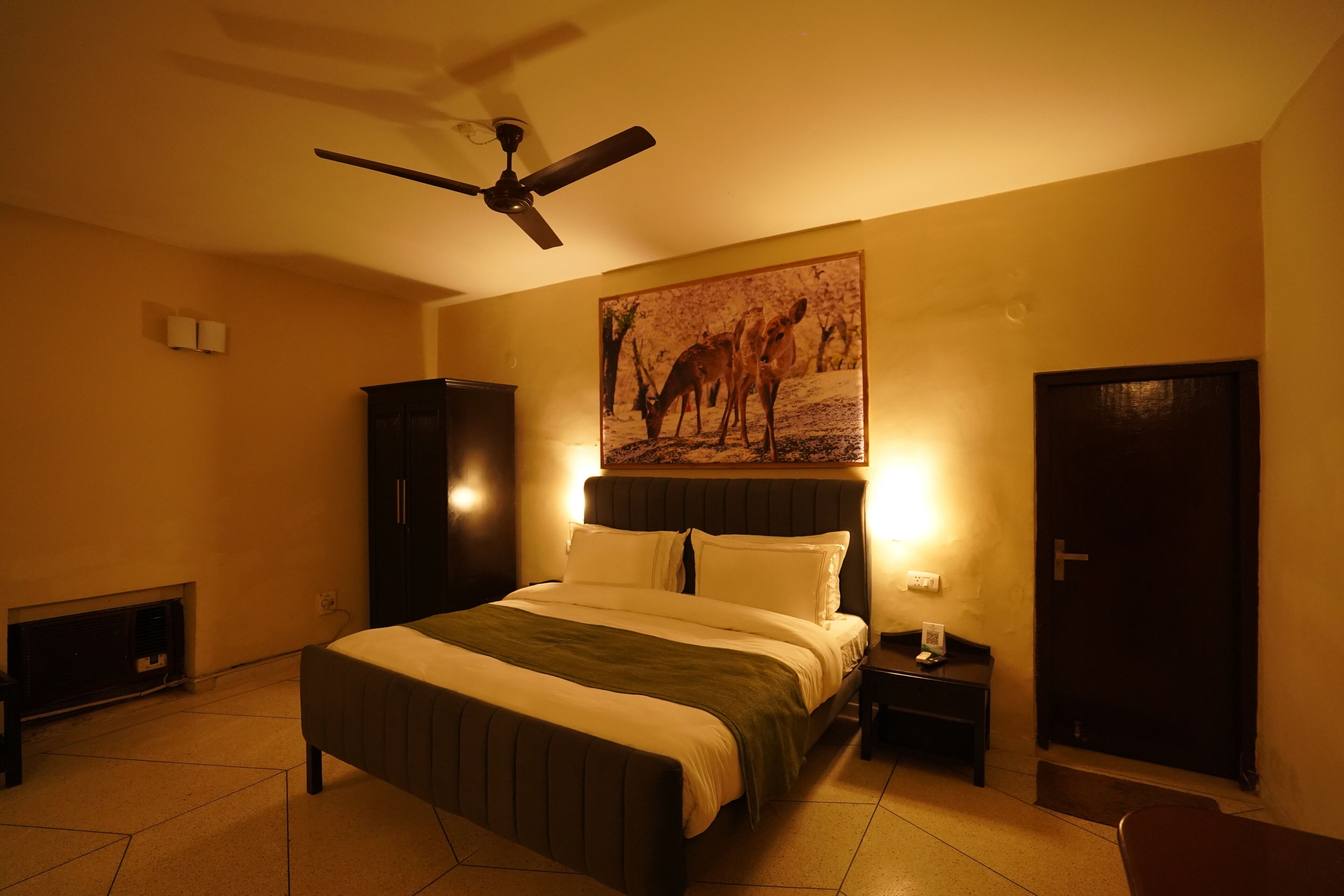A bedroom with a bed, a ceiling fan, a wall-mounted painting, bedside lamps, and a door.