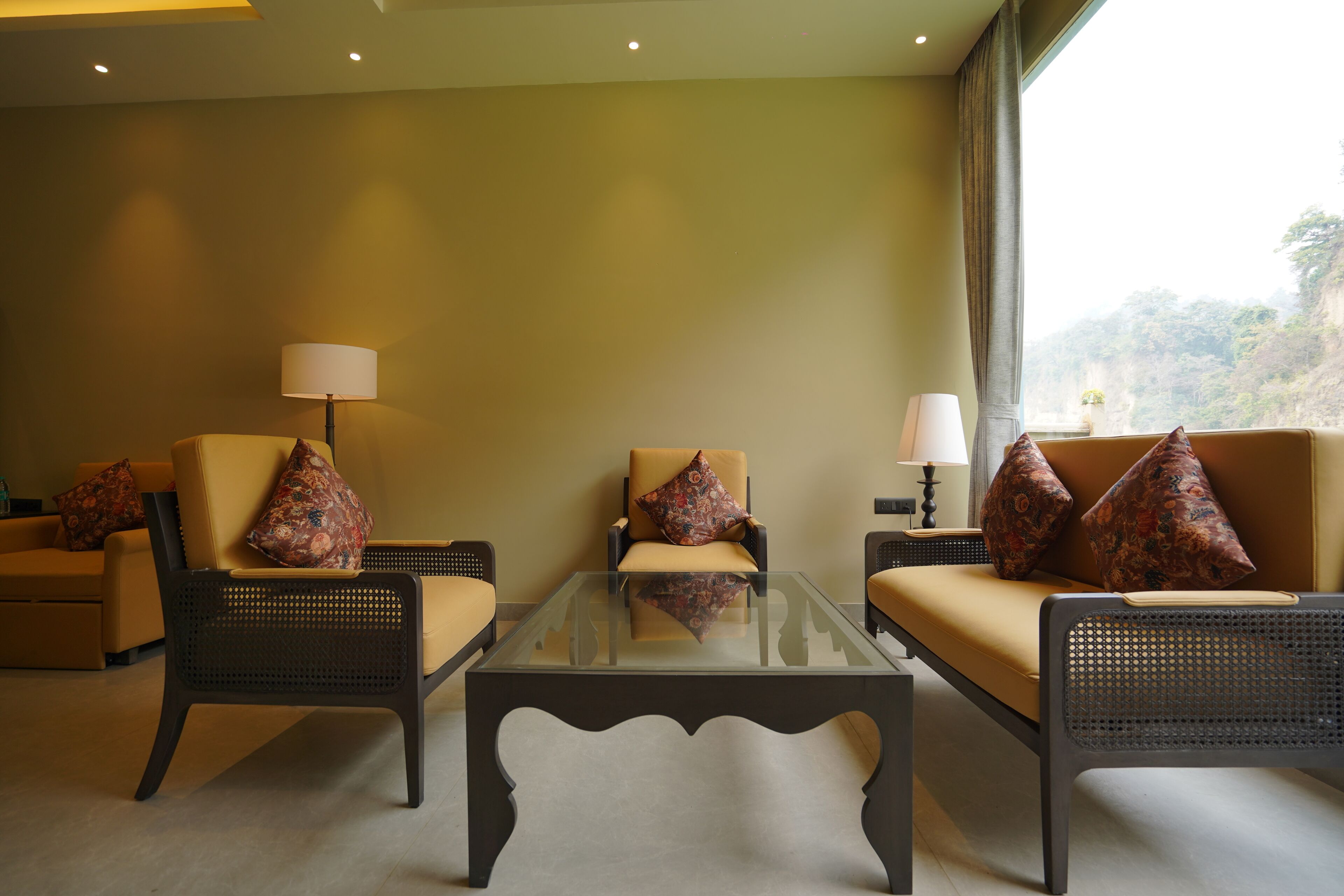A room with a sofa, two armchairs, a glass coffee table, and two lamps.