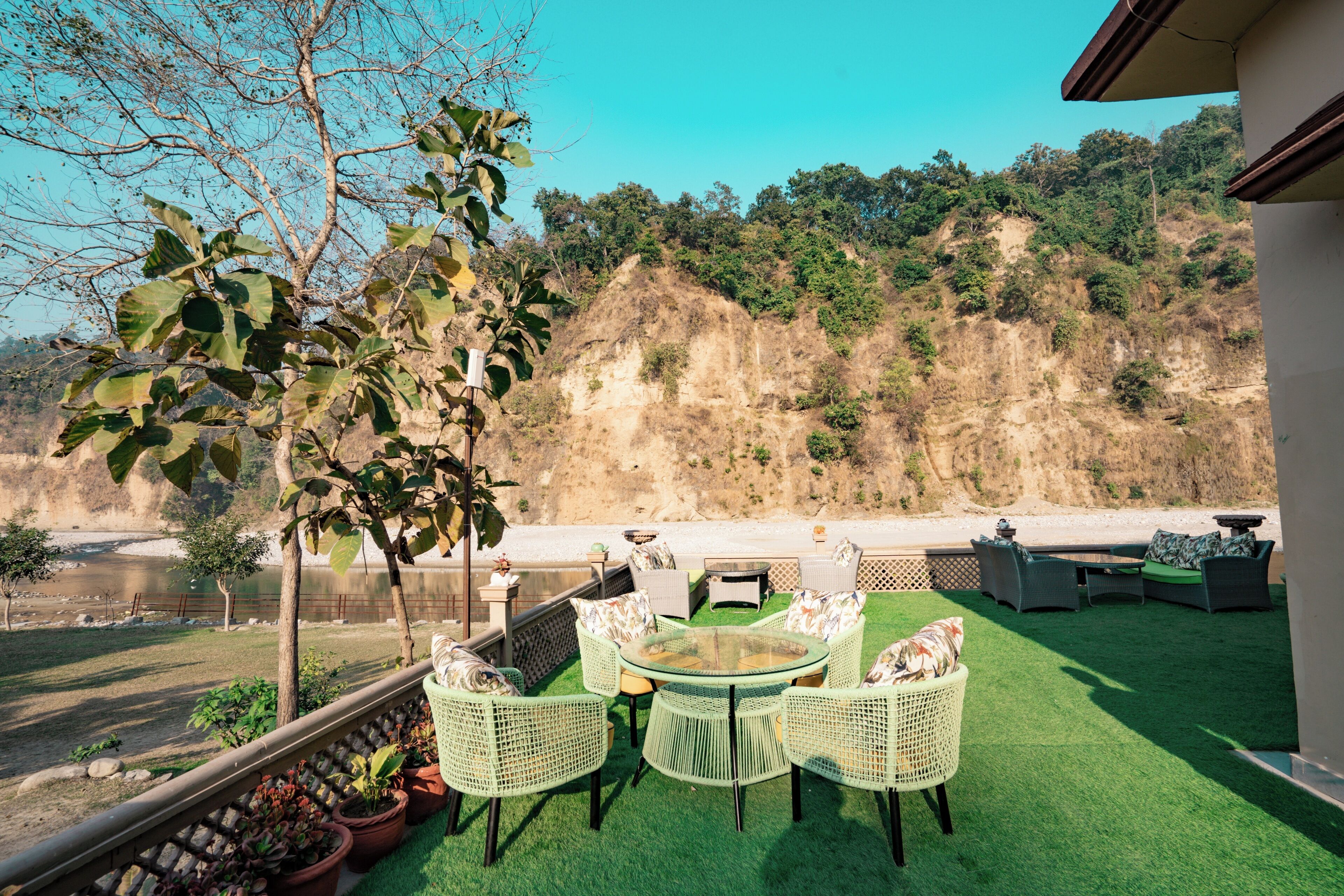 An outdoor patio with green artificial grass, wicker furniture, and a view of a river and hills.