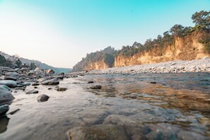 Une rivière aux eaux claires, bordée de rochers et d’une falaise boisée.