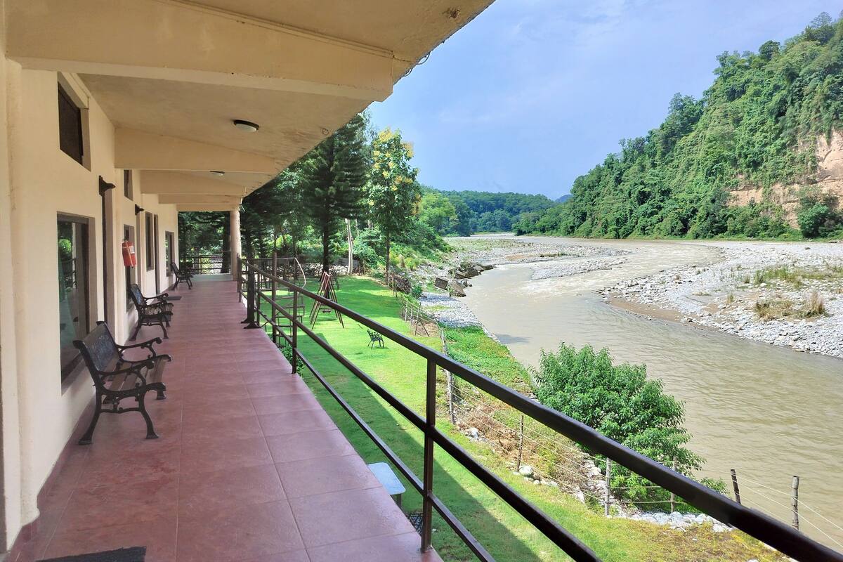 A covered outdoor area with benches, a railing, and a view of a river and forested hills.