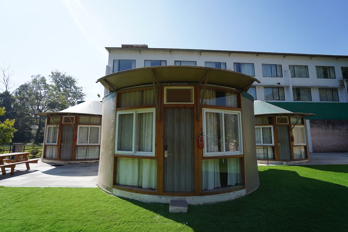 A small, single-story building with a curved roof and large windows, surrounded by a well-maintained lawn and a picnic table.