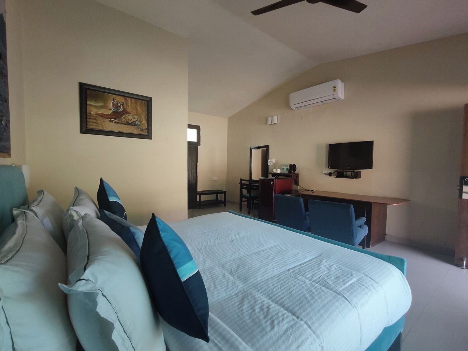 A hotel room with a bed, pillows, a desk with a chair, a television, and an air conditioning unit.